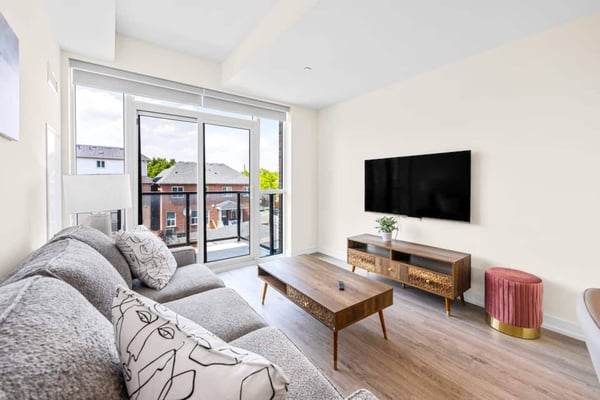Open-plan studio with dark blue accent wall, black sectional sofa, wall-mounted TV, and light wood kitchen with island seating