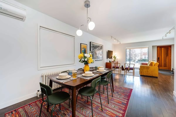 Modern kitchen with white cabinetry, stainless steel appliances, hexagonal tile backsplash, and open-plan dining area with wooden table and green upholstered